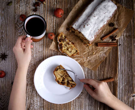 hand with a mug of tea and a piece of table on a plate and stollen on a wooden table. selective focusの写真素材