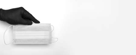 hand in a black latex glove holds a medical mask on a white background. High quality photoの写真素材