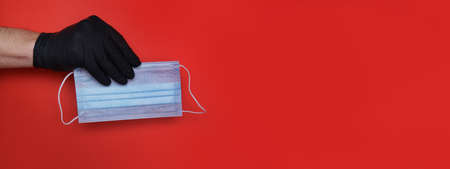 hand in a black latex glove holds a medical mask on a red background. High quality photoの写真素材