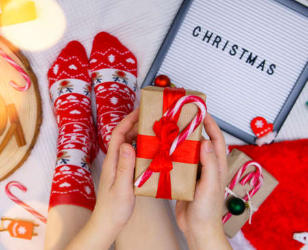 letter board with the inscription Christmas, feet in red socks and hands holding a box with a gift. selective focusの写真素材