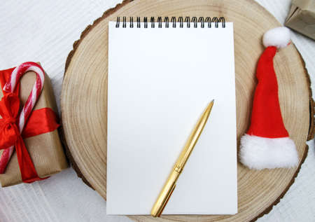 on the cut of the tree lies notebook, pen and Santa hat, and next to it is box with gift and candy...
