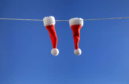 2 little Santa hats hanging on a rope against a blue sky. close-up, Merry Christmass celebrationの写真素材