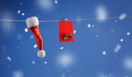 Santa hat and red plastic card with new year design hanging on a string on a blue backgroundの写真素材