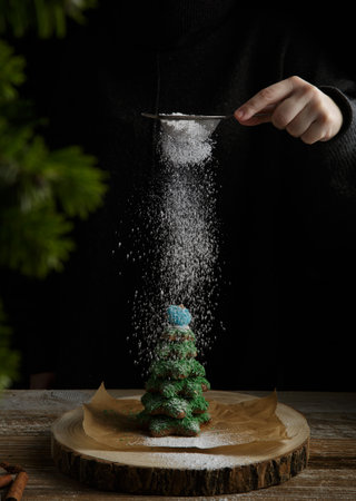 hand sprinkles icing sugar on gingerbread tree on dark background. holiday and Christmas concept. High quality photoの写真素材