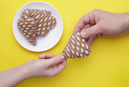 cropped image girl hand giving heart-shaped gingerbread to man hand on the yellow background. selective focus.High quality photoの写真素材