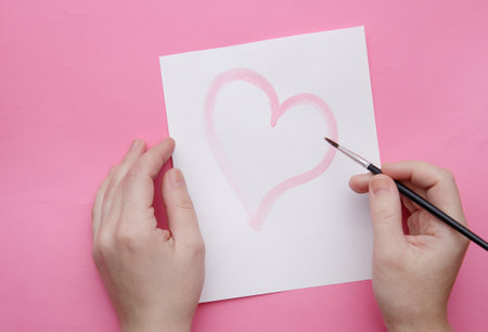 the hands of a girl who draws a heart with a brush on a sheet white of paper.selective focus. High quality photoの写真素材