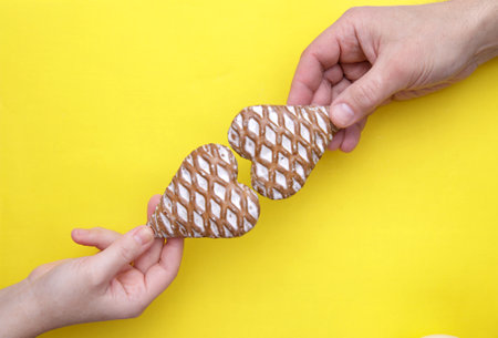 male and female hands hold out two heart-shaped gingerbread to each other on the yellow...