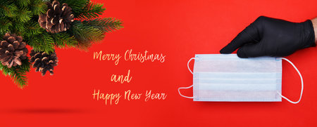 hand in a nitrile glove holds a disposable mask and wishes for a merry Christmas on a red background. selective focus.High quality photoの写真素材