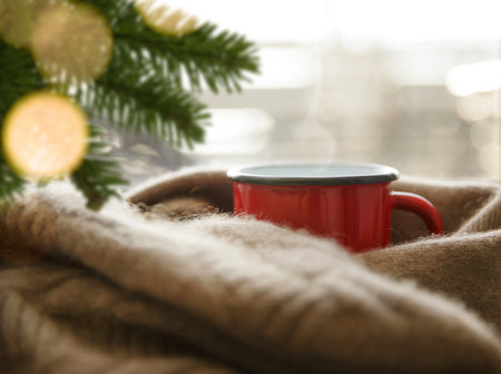 hot drink in a red metal mug wrapped in a cashmere scarf on a cold day under spruce branchesの写真素材