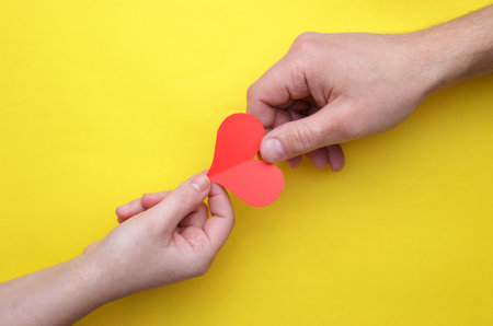 Man hand gives paper heart woman in hand on a yellow background. selective focus .High quality photoの写真素材