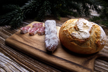 bread and sausage lie on a wooden board. in the background there are spruce branchesの写真素材