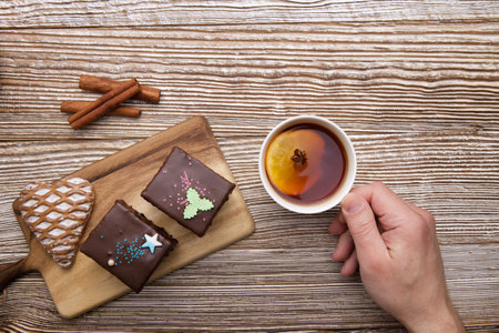 Male hand holding cup with fruit tea and fresh gingerbread on wooden background. selective focus .High quality photoの写真素材