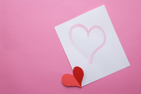 paper cut red heart lies next to leaf with pattern of hearts on pink background. selective focus .High quality photoの写真素材