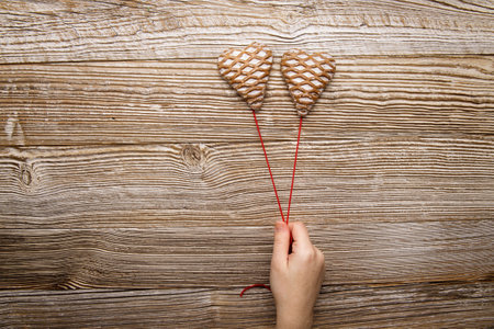 hand holds two gingerbread in the form of hearts on a red thread on a wooden background. selective focus. High quality photoの写真素材