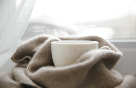 A hot drink on the window on a cold frosty day is on the windowsill next to a cashmere handkerchief on a cold frosty day. High quality photoの写真素材