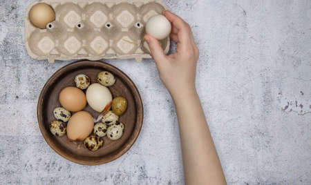 hands of invisible person carry fresh chicken and quail eggs from brown clay plate to egg tray. gray table. top view. High quality photoの写真素材