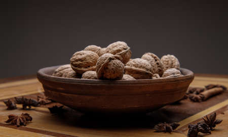 Nuts. whole walnuts in an earthenware dish on a dark wooden table near cinnamon and star anise. selective soft focus.の写真素材