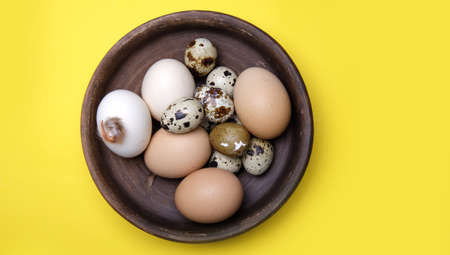 fresh quail and chicken eggs from the farm in a brown clay plate on a yellow background. selective soft focus. top viewの写真素材