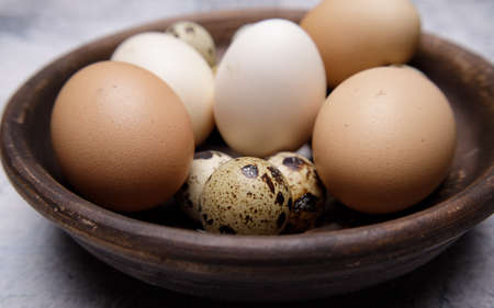 fresh quail and chicken eggs from the farm in a brown clay plate on a gray marble table. selective soft focus. High quality photoの写真素材