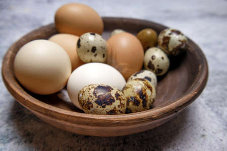fresh quail and chicken eggs from the farm in a brown clay plate on a gray marble table. selective soft focus. High quality photoの写真素材