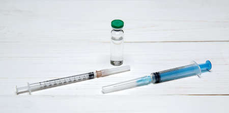 two syringes for injections and bottle with a vaccine lie on light wooden table. selective focus.High quality photoの写真素材