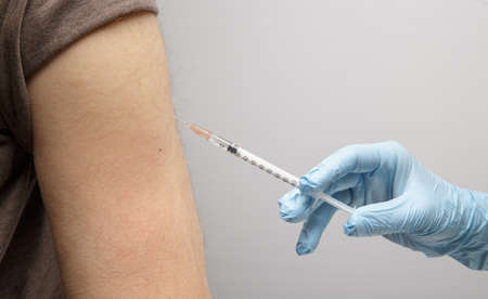 the hand of a paramedic makes an injection of a vaccine to an invisible person. health concept. protection against coronavirusの写真素材