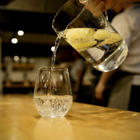 hand of an invisible waiter pouring from a glass carafe of lemonade into a glass. selective focus. High quality photoの写真素材