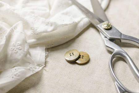 tailors scissors lie on top of the cambric. Nearby are two wooden buttons.selective focus. High quality photoの写真素材