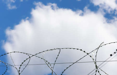 barbed wire as a restriction . Against the backdrop of a bright blue sky with clouds. High quality photoの写真素材