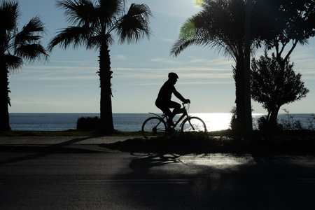 silhouette of a Man riding a bicycle against the backdrop of a sea sunset. The concept of nature and beauty. Orange sunset. Silhouette at sunset. High quality photoの写真素材
