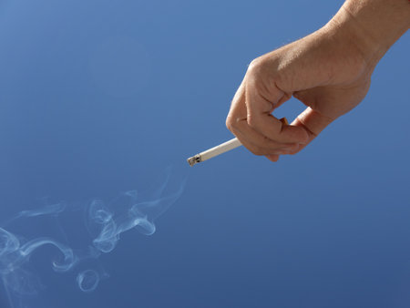 cigarette in man hand against a blue sky. close up. High quality photoの写真素材