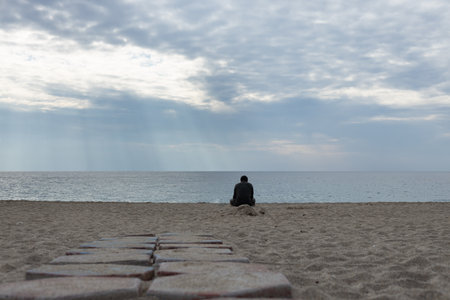 Rear view portrait of a man relaxing sitting on the beach and looking at the sea in the background....