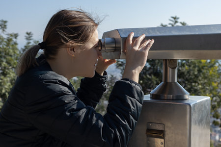 Girl tourist uses panoramic sightseeing binoculars to survey the area. High quality photo