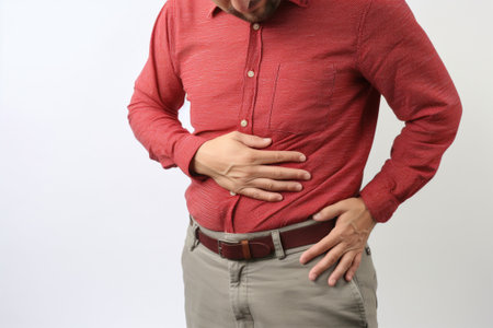A man in a red shirt suffering from stomach pain holds his stomach with his handsの素材