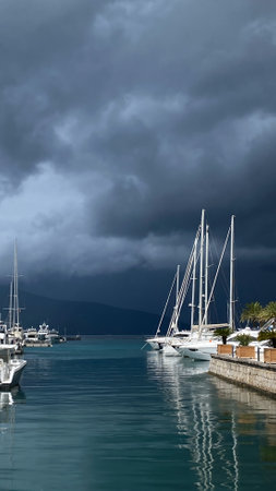 May 22, 2024, Tivat, Montenegro.A marina with several moored sailboats and yachts under dark storm clouds. The water is calm and reflective, creating a serene contrast to the ominous sky. Copy spaceのeditorial素材