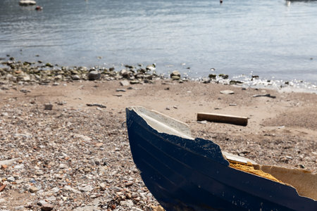Broken blue boat on a pebble beach with the sea in the background. the aftermath of a storm on a sunny day. Copy space.Suitable for nature or abstract contentの写真素材