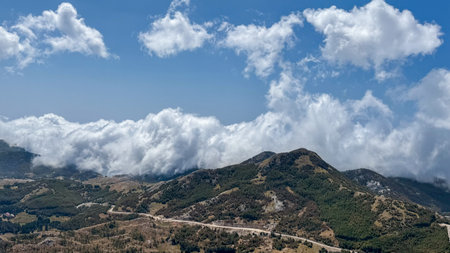 A sweeping view of a mountainous landscape with lush green hills, partially covered by low-hanging...