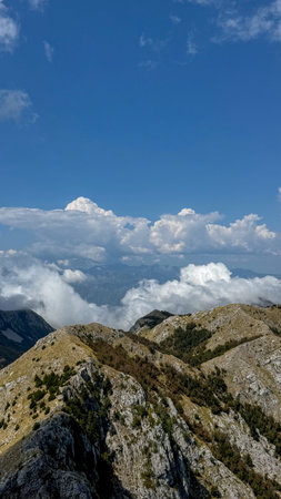 A wide view of a rugged mountain ridge, with rocky outcrops and sparse vegetation, set under a vast,...