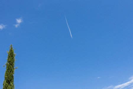 A blurry high-flying passenger plane and white streaks in the blue sky.の写真素材