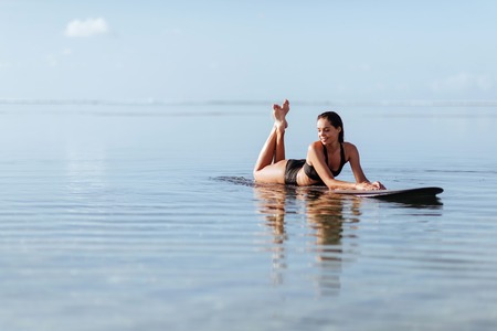 Woman smiles and sits on the surfboard in the ocean.の写真素材