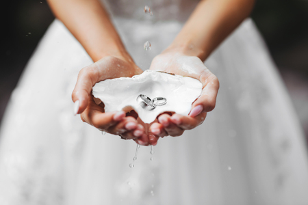 Hands, dressing a wedding ring, rings in the sand, rings on the shell.の写真素材
