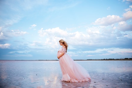 beautiful young pregnant woman enjoying the sun on pink lakeの写真素材