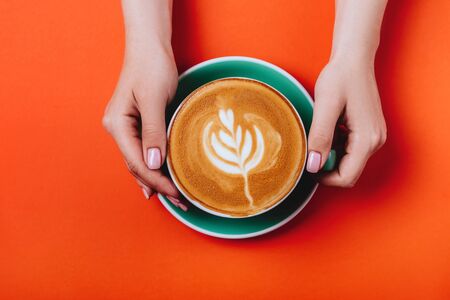 Female hands with a coffee cappuccino cyan cup. Sunny orange toned photo.の写真素材