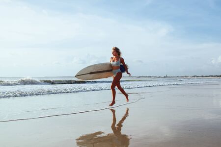 Surfer girl walking with board on the sandy beach.の写真素材