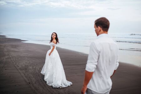 Elegant gorgeous bride and groom walking on ocean beach during sunset time.の写真素材
