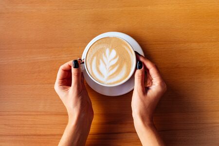Female hands with cup of hot tasty coffee in cafeの写真素材