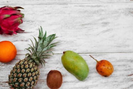 Tropical fruits lie on a wooden white surface.