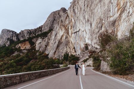 Young newly wed couple, bride and groom kissing, hugging on perfect view of mountains, wedding conceptの写真素材