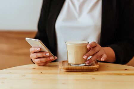 womans hand holding cell phone while drinking coffeeの写真素材