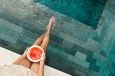 Girl holding watermelon in the blue pool, slim legsの写真素材